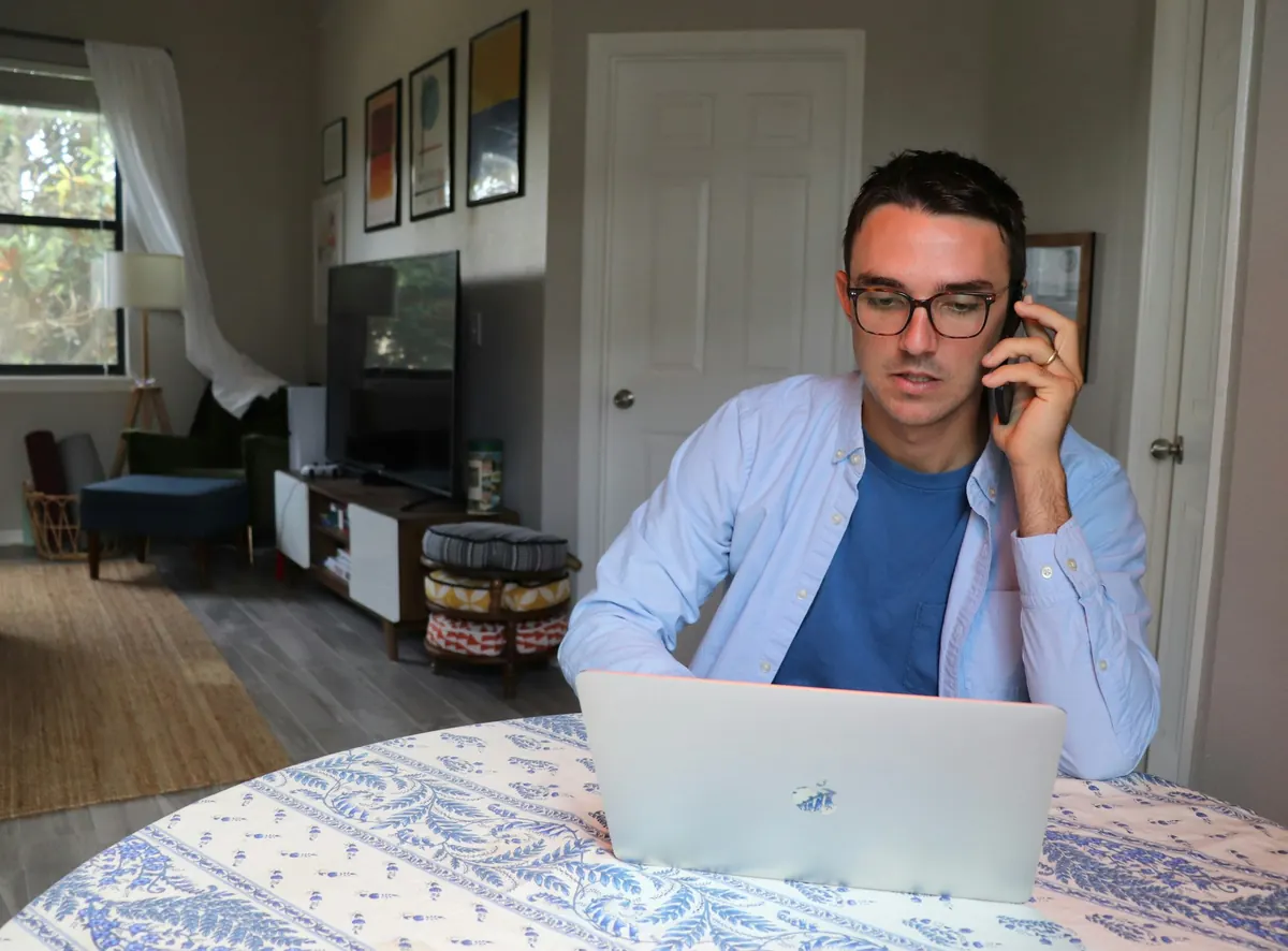 A man on the phone at a laptop in a home office